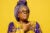 Opal Lee wears a purple and gold dress and headscarf, with one hand over her heart.
