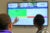 Three people look and point at a large TV monitor showing diagrams in the LoveMyAir interface.