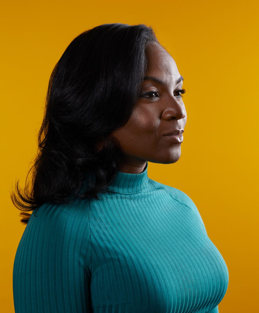 Kizzmekia Corbett wearing a longsleeve, teal turtleneck dress, looks off camera with a serious and powerful expression.