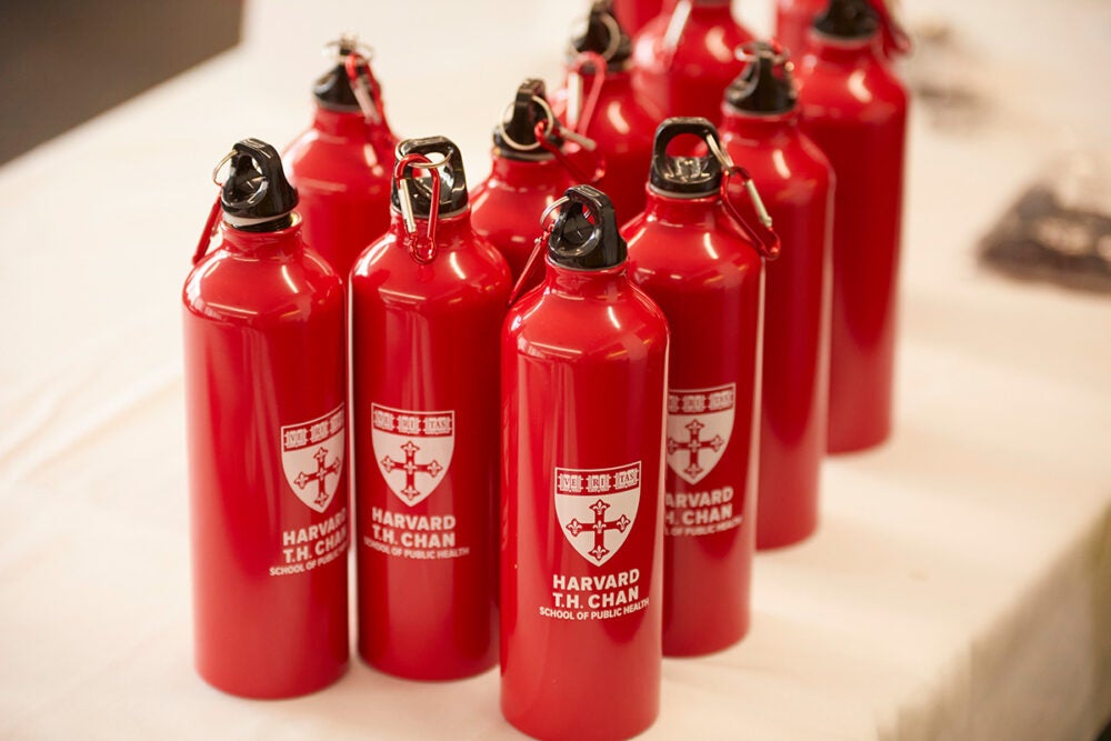 Collection of metal red Harvard Chan water bottles with black tops with red carribeaners sit on a white table.
