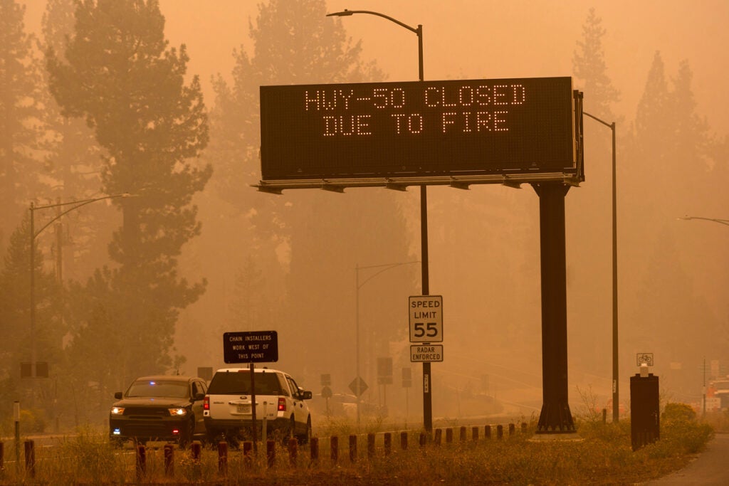 A highway is shroweded in yellow haze. A digital highway sign says "HWY-50 closed due to fire."