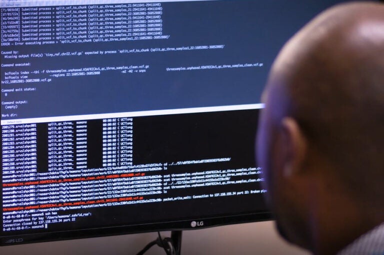 A man sits at a computer screen with rows of code.