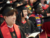 Three students in Harvard Chan regalia sitting in a stadium and smiling.