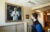 A male student wearing a blue shirt, black vest and black facemask walks past a portrait of Bernard Lown.