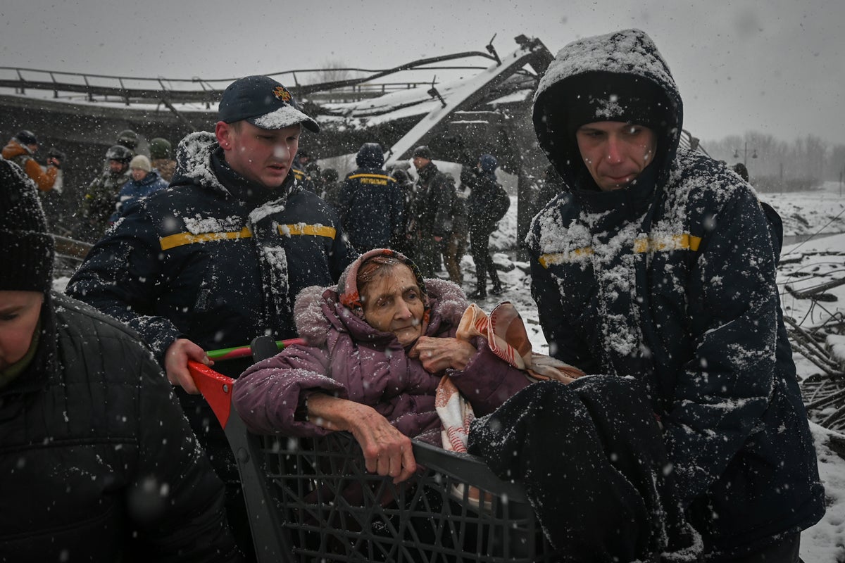 An eldery woman is carried by two male aid workers wearing dark parkas outside in the snow in Ukraine.