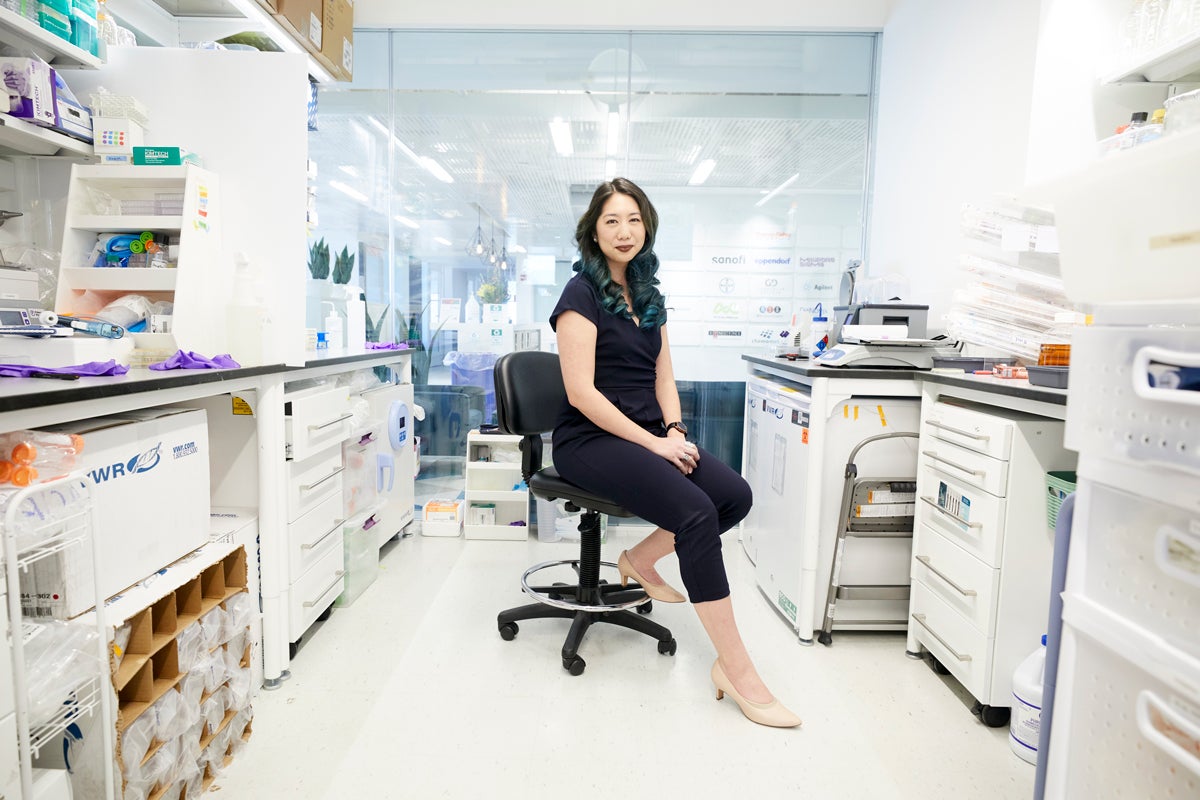 Minmin Yen, seated and wearing a black short-sleeved jumpsuit, sits in a black lab chair in the middle of her white lab at PhagePro.