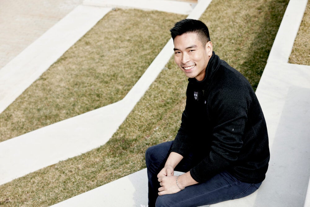 Tanat Chinbunchorn, wearing a black fleece and blue jeans, sits on grassy steps by Countway library and smiles at the camera.