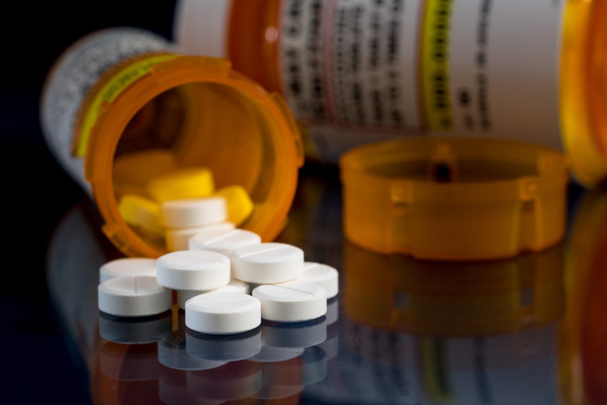 A bunch of white round pills spill out of a nondescript orange pill bottle against a black background. (stock photo)