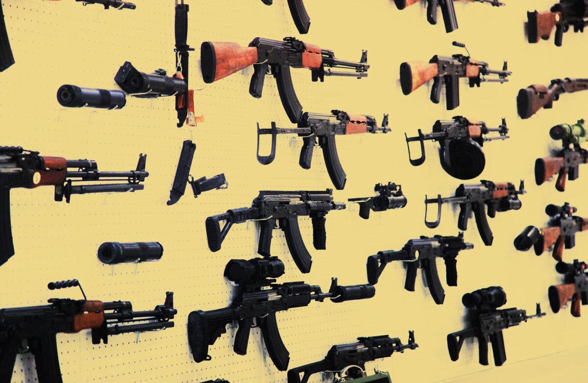 Assault rifles hang on a yellow pegboard.