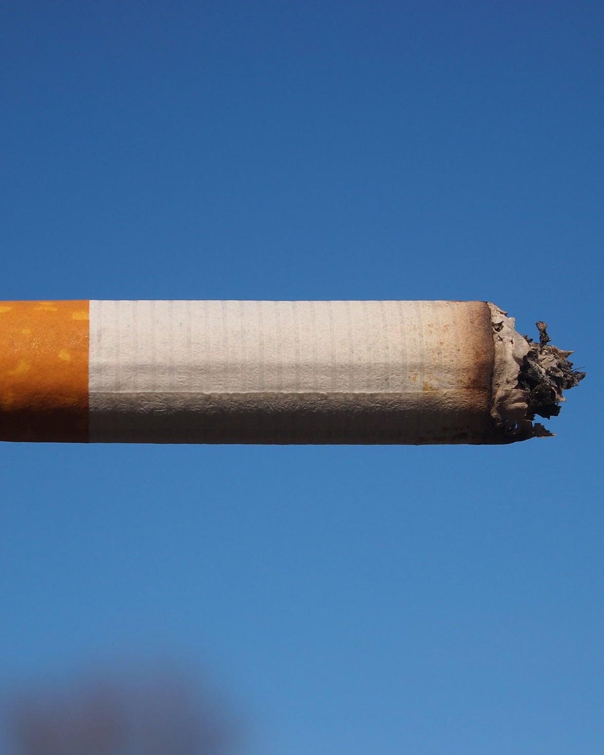 A partially used cigarette against a blue sky.