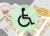 Photo Illustration: A unspecific zoning map is shaded with grays, tans, and pinks. A black wheelchair symbol (traditional ADA symbol) sits on a light green opaque circle.