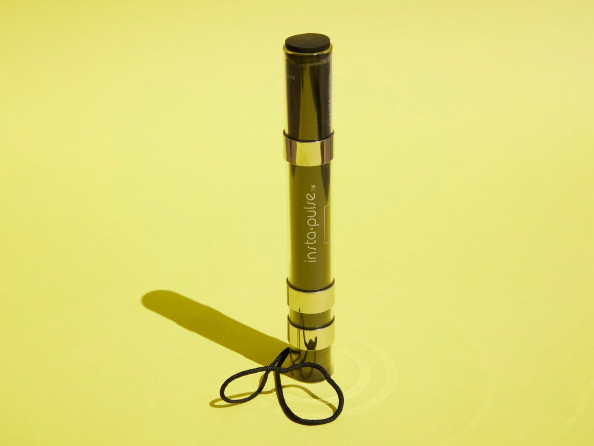 A black tubular device, about the size of a flashlight, sits vertically on a yellow bright yellow background and casts a harsh shadow. The device has two silver bands and the text "insta-pulse" in the middle.