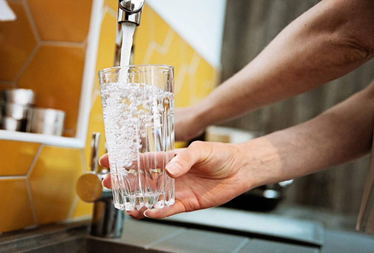 Two hands fill up a glass of water at a silver facet.