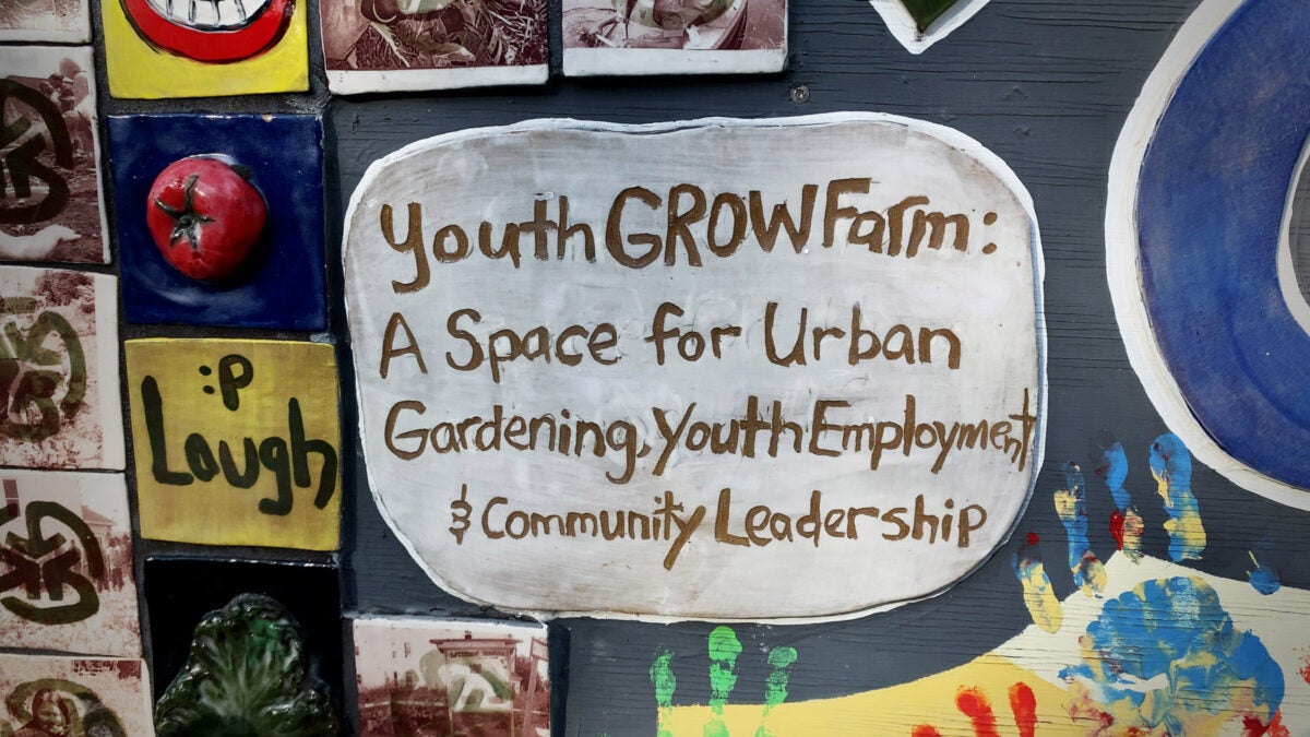 A close-up of a mosaic mural. The main tile, great with green text, reads “YouthGROWfarm: A space for urban gardening, youth employment & community leadership.”