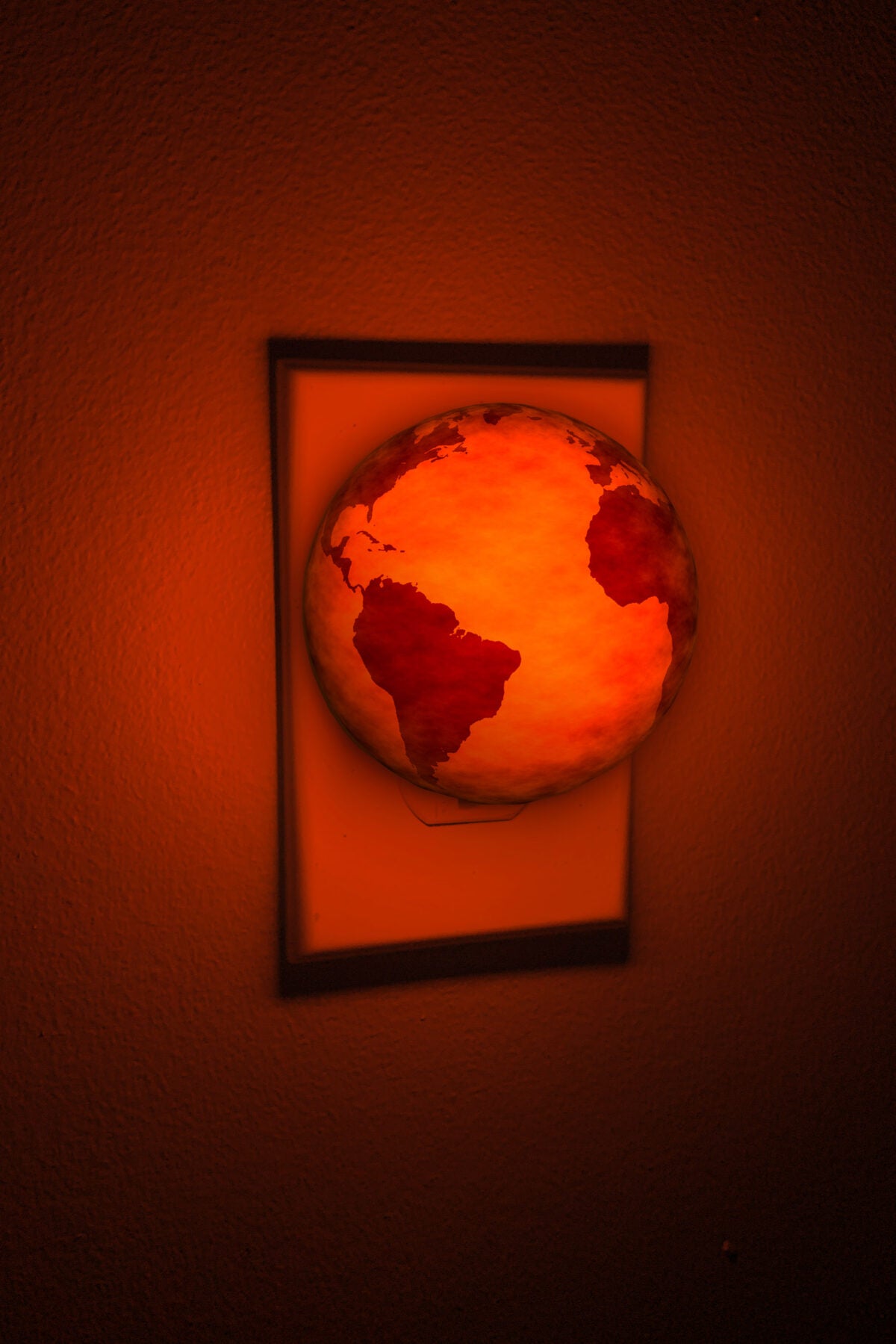 Photo illustration: A red-orange glowing earth acts as a nightlight in a room. The light emits a bright red-orange glow.