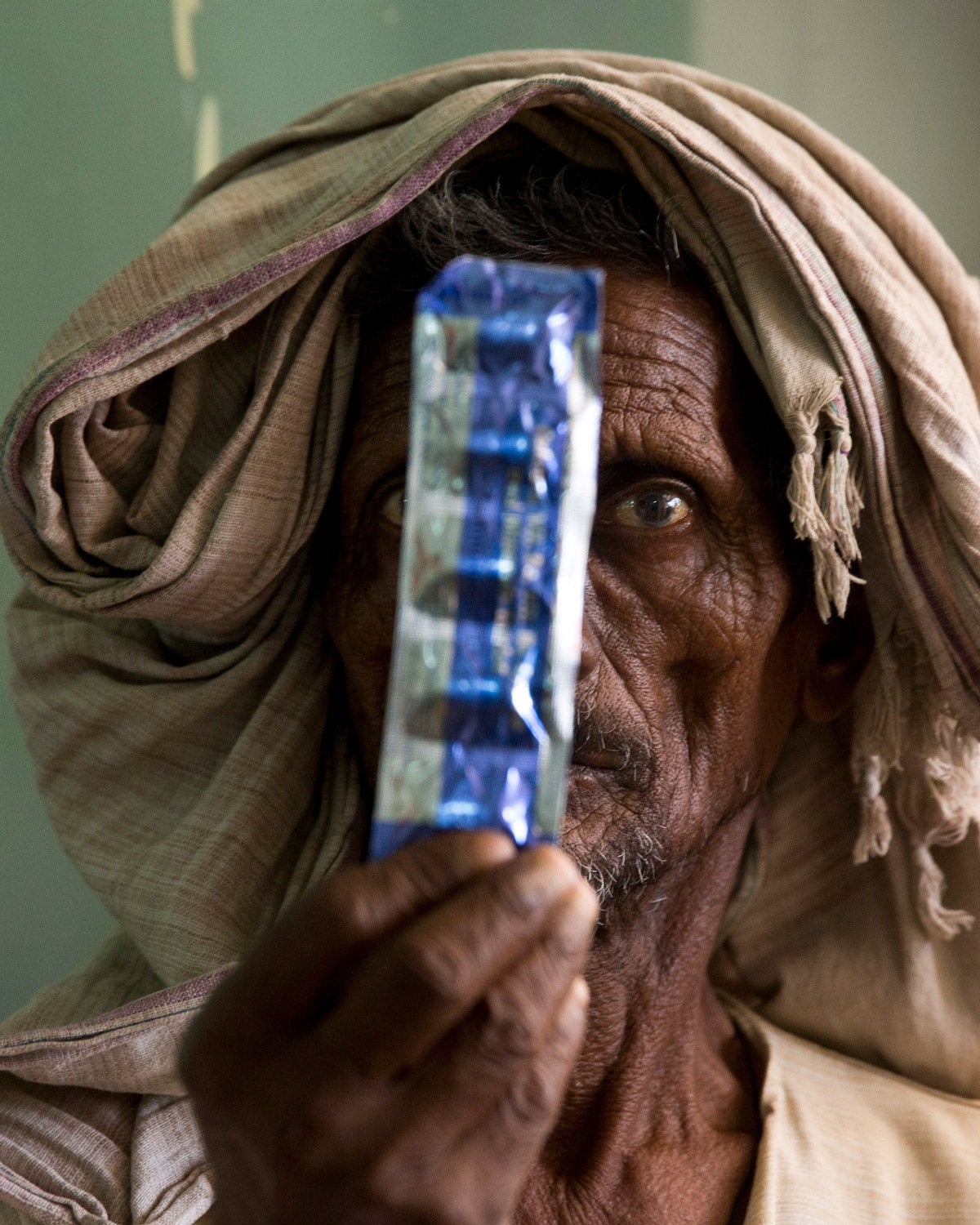 A male tuberculosis patient holds a strip of blue packaged medicines, covering the left part of his face, at a hospital in India.