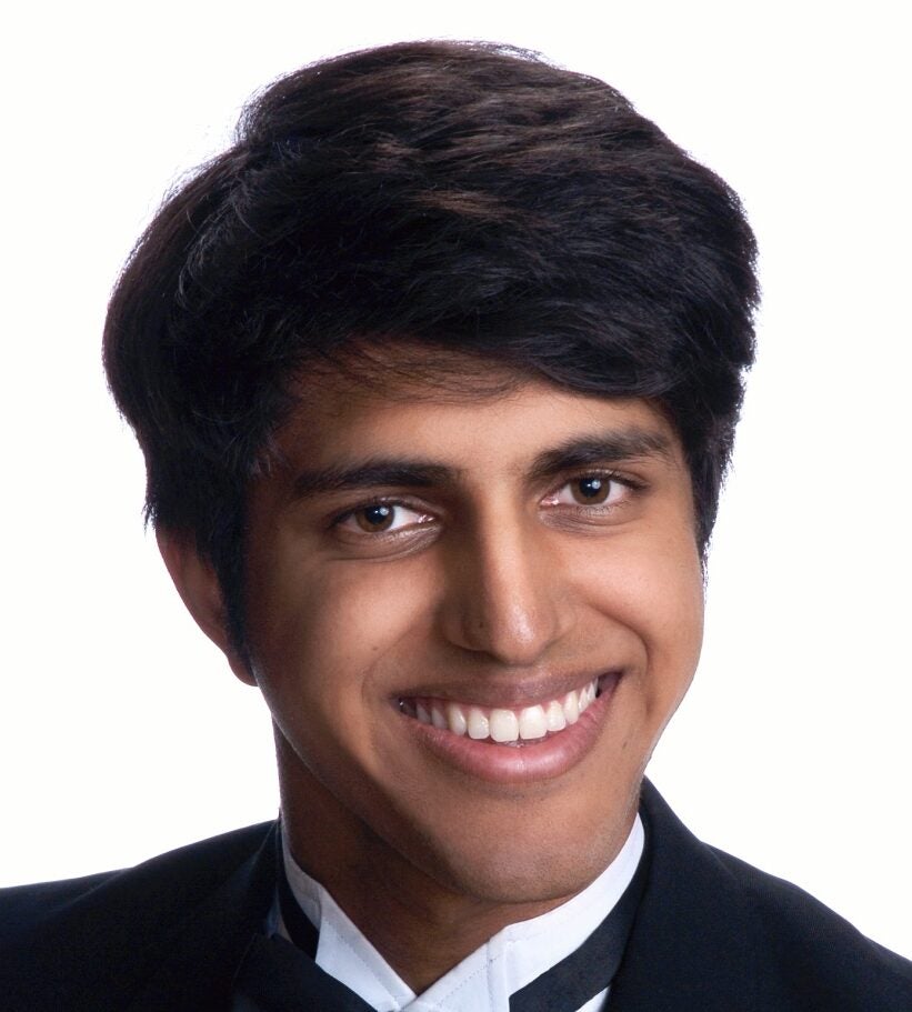 Simar Bijaj smiles facing the camera. A close headshot, Bajaj wears a white collared shirt and black jacket.