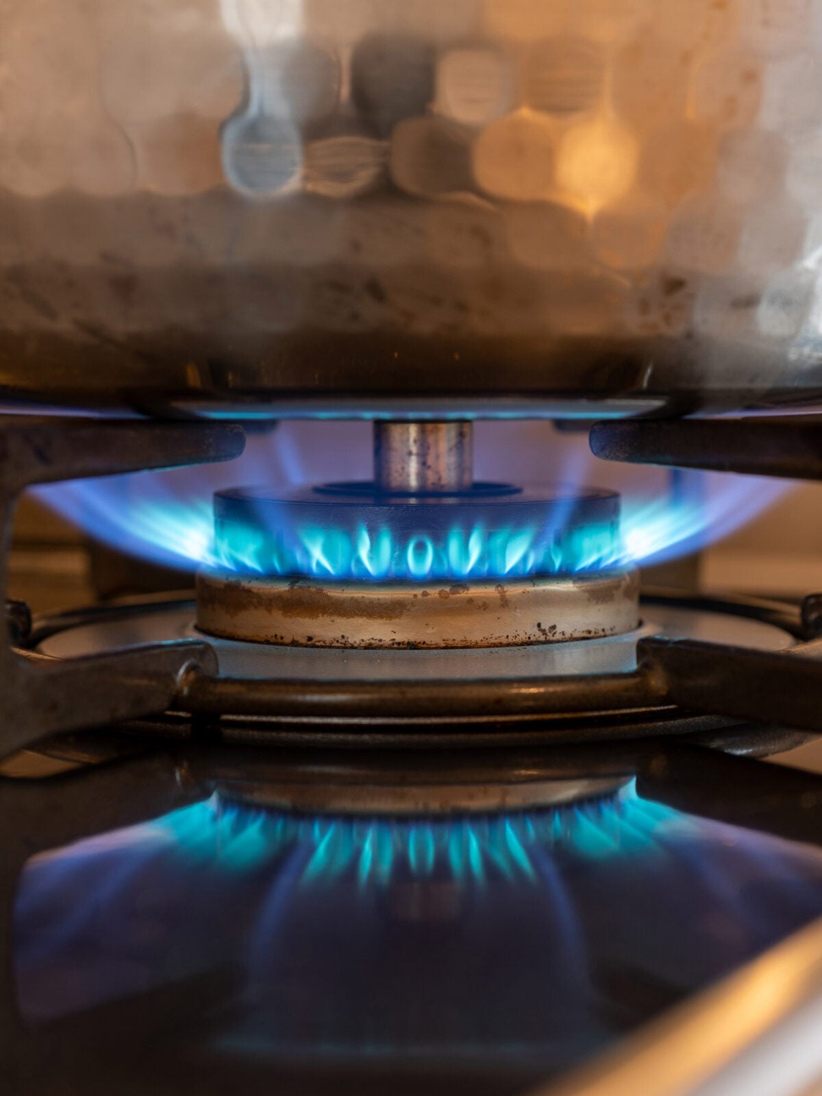 A textured pot sits upon a blue gas flame on a stove top.