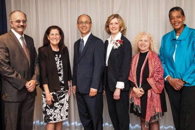 Six people wearing formal wear stand infant of a white curtain and pose of a photo. Three are 2002 Harvard Chan Alumni Award winners (from left to right) Wafaie Fawzi, Julie Buring, and Stephen Hwang, with Lois B. Travis (2021 Award of Merit recipient), Kathleen Kahn (2020 Award of Merit recipient), and Dean Michelle A. Williams.