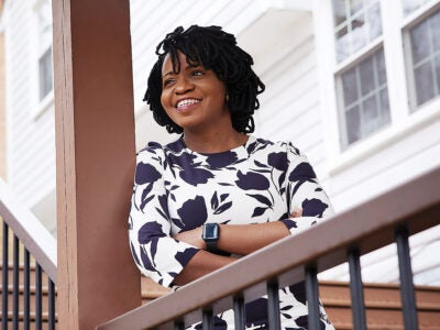 Anuoluwa Ishola leaning against a porch beam smiles broadly while looking off-camera.