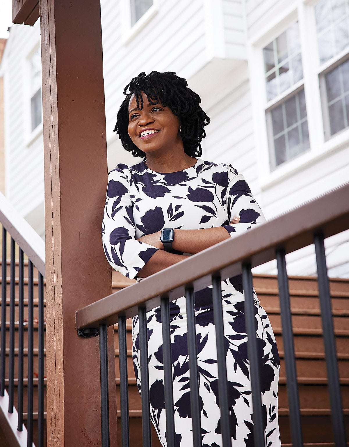 Anuoluwa Ishola leaning against a porch beam smiles broadly while looking off-camera.