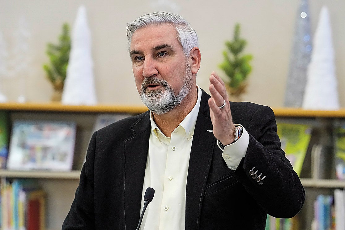 Eric Holcomb speaking at a podium wearing a white button down and dark blazer.