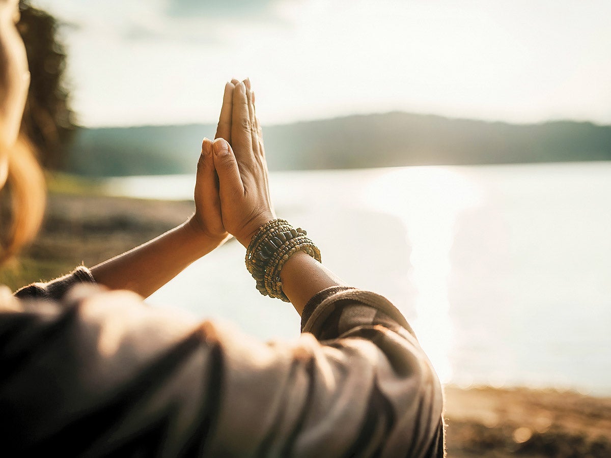 Two hands in a flat-palm prayer position by a nondescript lake and beach.