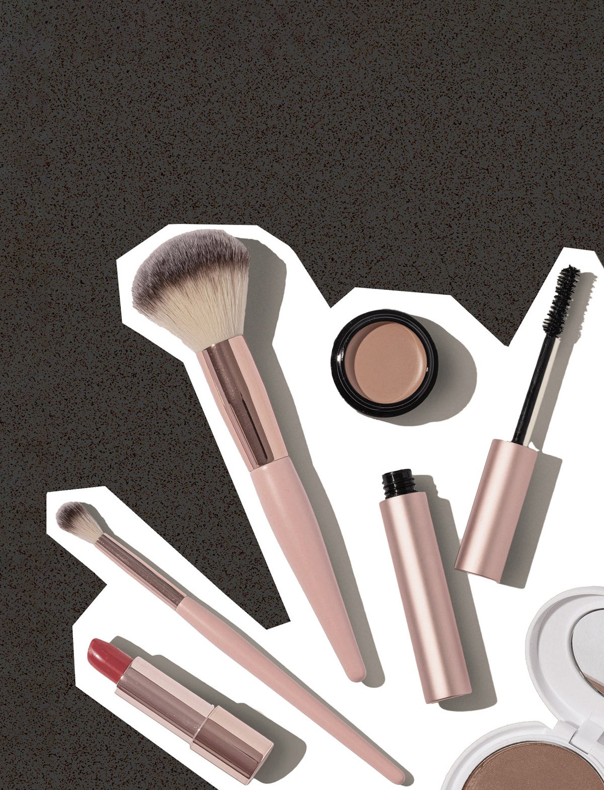 Miscellaneous rose gold cosmetic products are placed against a grey-speckled background.