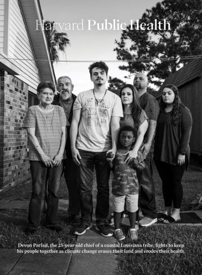 Cover of Harvard Public Health, Spring 2023. Photo: Black and white photo: Seven family members stand close together and stare directly into the camera. In the center is a twenty-something man, who holds the hand of a young black boy. To his left are an elderly man and woman. To his right are a middle-aged woman who holds the young boy's other hand, a middle-aged man, and a young woman. They stand in a backyard, with a grill and house on one side, and a modern tipi on the other. Text reads: Devon Parfait, the 25-year-old chief of a coastal Louisiana tribe, fights to keep his people together as climate change erases their land and erodes their health.