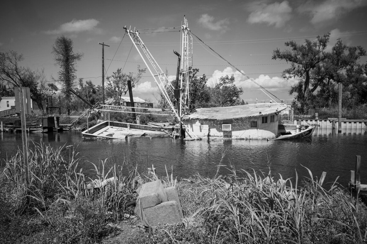 Black and white photo: A destroyed fishing boat is partially submerged in water in a Louisiana marsh.