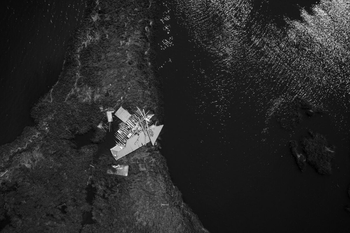 Black and white aerial drone photo: A single destroyed house on a peninsula in the Louisana bayou.