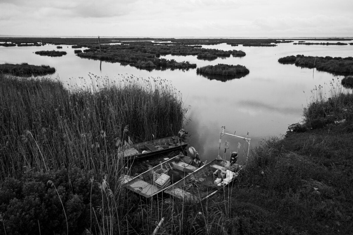 Black and white photo: Two aluminum boats rest along the shoreline of a marshy shoreline in Louisiana.
