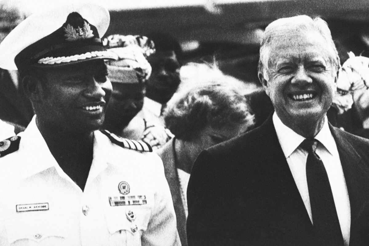 Black and white archival photo: Jimmy Carter stands next to the governor of Lagos State, Captain Mike Ahigbe. Carter wears a suit. Ahigbe is in a white military uniform.