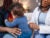 A black female healthcare worker visits a mother and son at their home. The healthcore worker checks his lungs with a stethoscope.