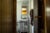 A walker sits in the doorway of a recently renovated bathroom with a new grey vanity, white mirror and lights. The sink is covered with standard bathroom items: toilet paper, contact solution, cleaner, etc. A brown towel hangs from a towel rod on the right.