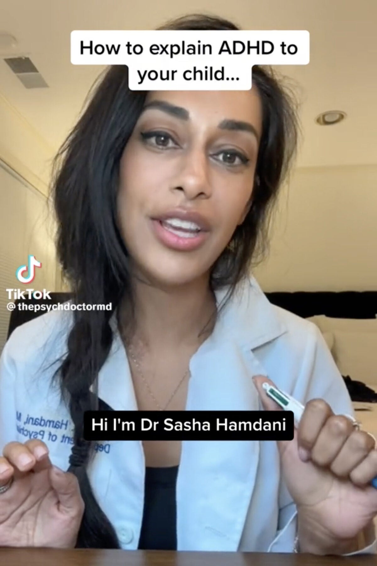 Still image capture from TikTok: A brown woman wearing a lab coat and hair in a single braid holds a four-colored pen and talks to the camera. The captions say “How to explain ADHD to your child…” and “Hi I’m Dr. Sasha Hamdani.”