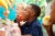 Two elementary-aged children eat apples in a school cafeteria. They are wearing blue-polo shirts and there is a bright mural in the background.