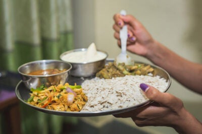 Two female hands hold a mental plate of Nepali food with Dar and sauces.
