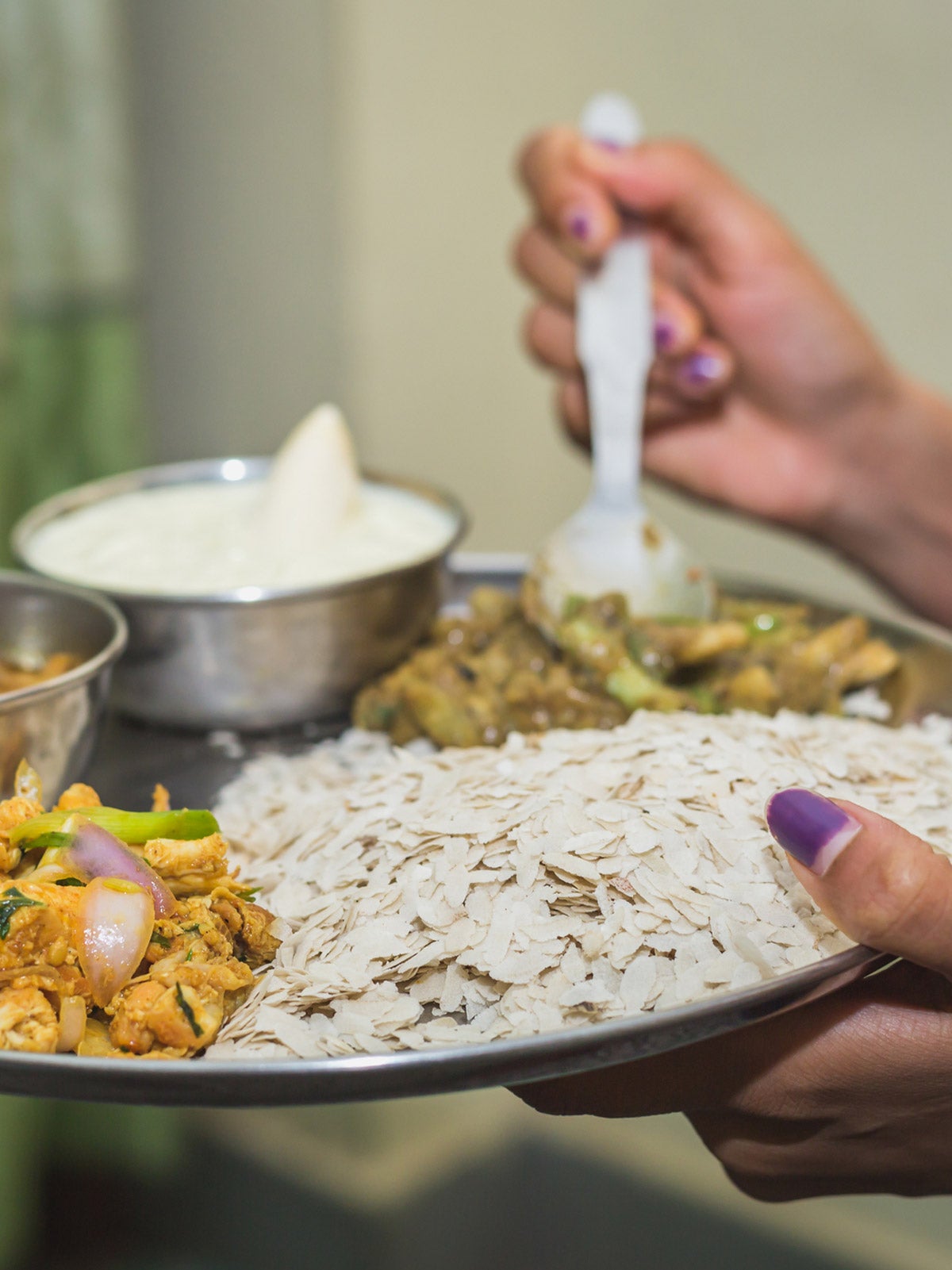 Two female hands hold a mental plate of Nepali food with Dar and sauces.