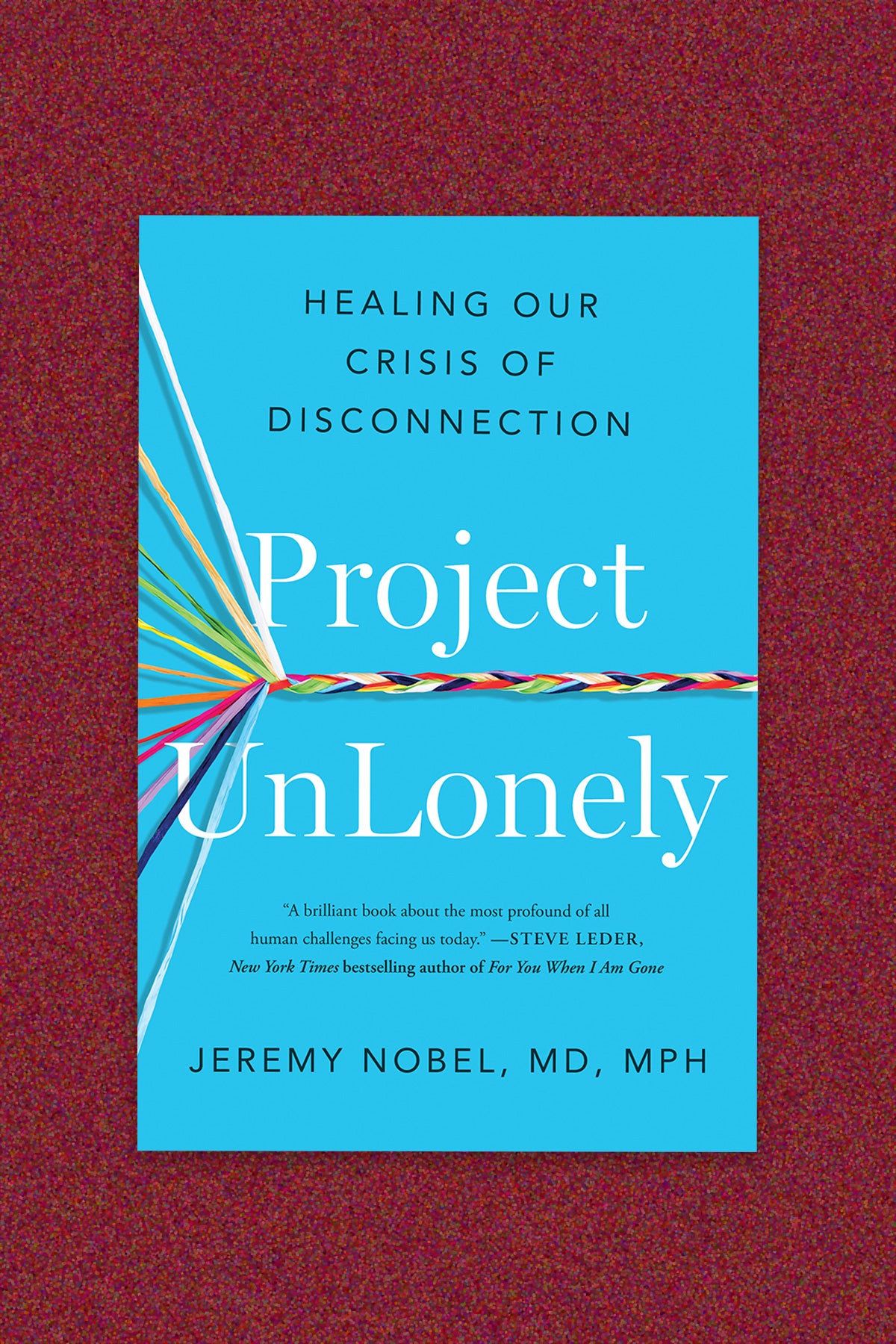 Book cover of “Project UnLonely: Healing our crisis of disconnection” by Jeremy Nobel, MD MPH. The book cover is a bright blue with white serif type for the title and black sans serif for subtitle and author name. Eleven individual colored threads enter from the left side of the cover and converge in a braided line that intersects the title in the middle of the cover. The book cover is on a deep red background.