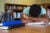 A teenager rests his head in his forearms and sleeps at a school library table. Three binders are on the table and his book bag sits in a chair.