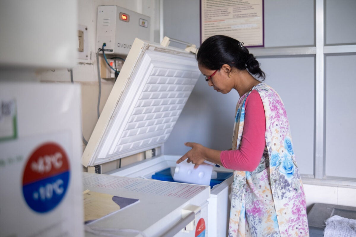 A female healthcare worker lifts a container of vaccines out of a white deep freeze at a health clinic in northeastern India.