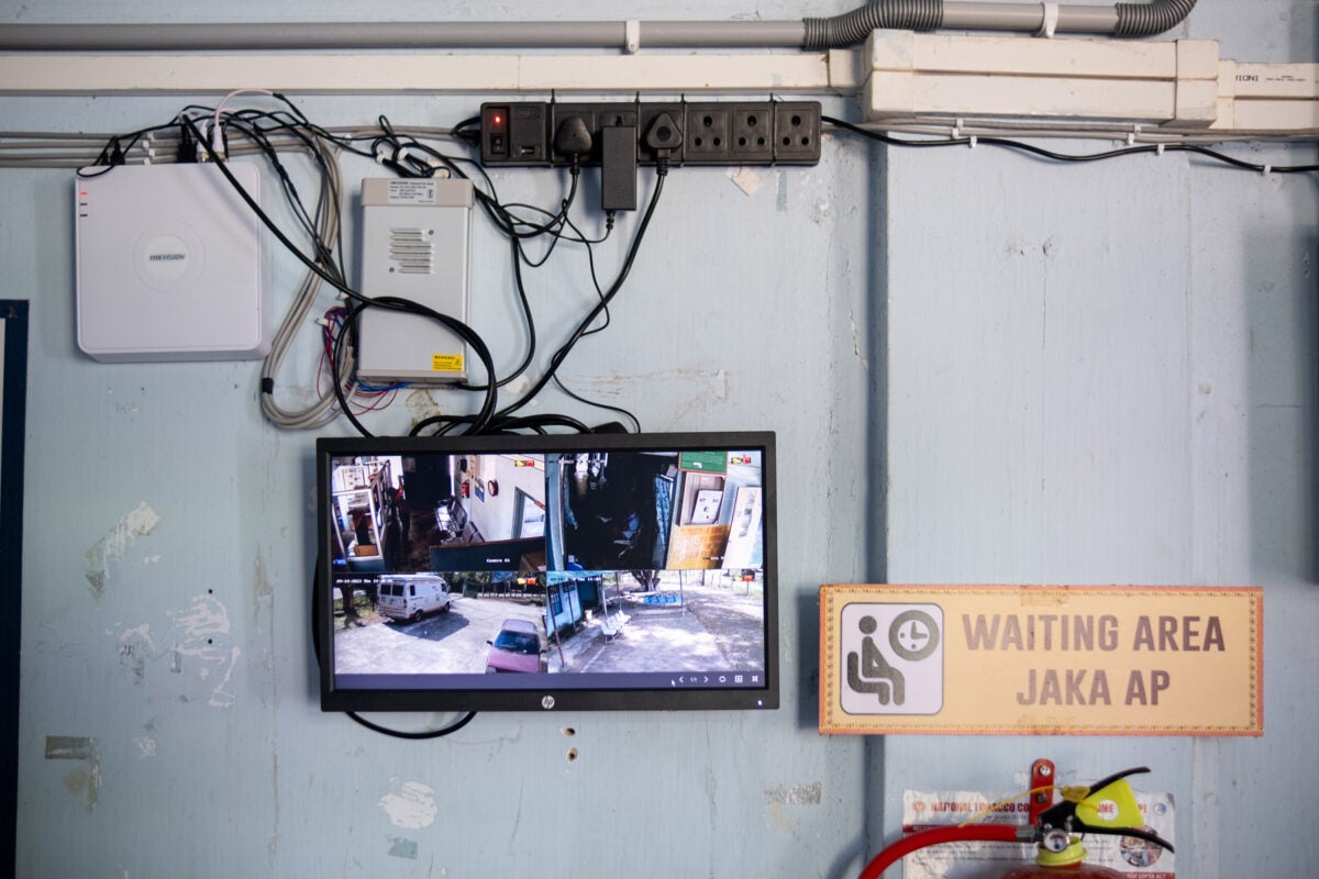 A CCTV screen hangs in the waiting area of a health clinic in northeastern India. Black and gray cords and a powerstrip hang above on the wall.
