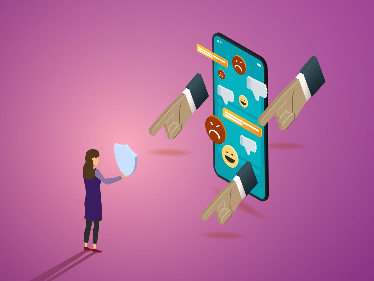 Illustration: A female figure holds a shield in front of her body, blocking an oversized phone with pointing fingers, dislike icons, menacing emojis and text messages. The composition is on a purple-pink background.