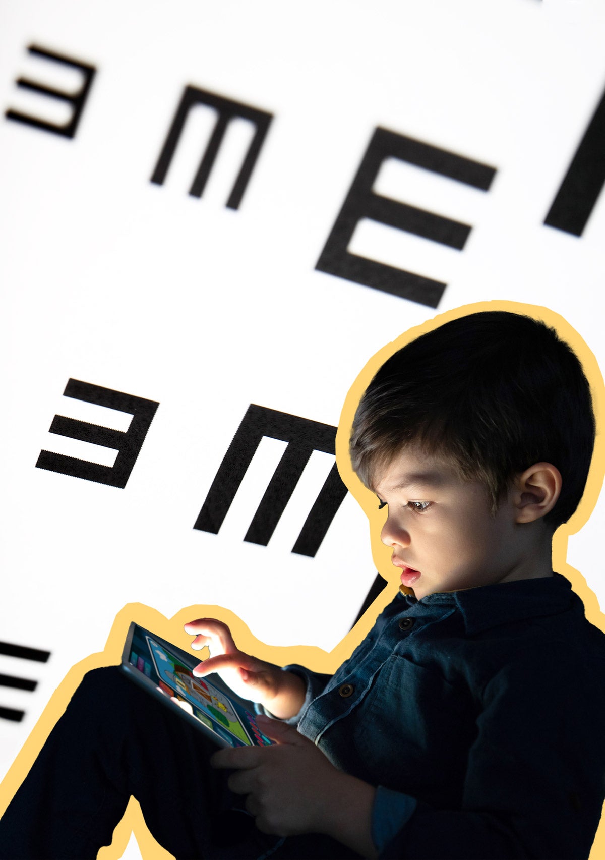 Photo illo: A young boy sits and plays with a glowing tablet. Behind him is an oversized eye chart that blurs on the sides.