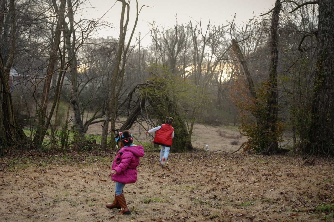 Two young black children play in their rural backyard near Memphis, Tenessee. One child wears a bright pink coat and jeans, the other a bright red vest and jeans.