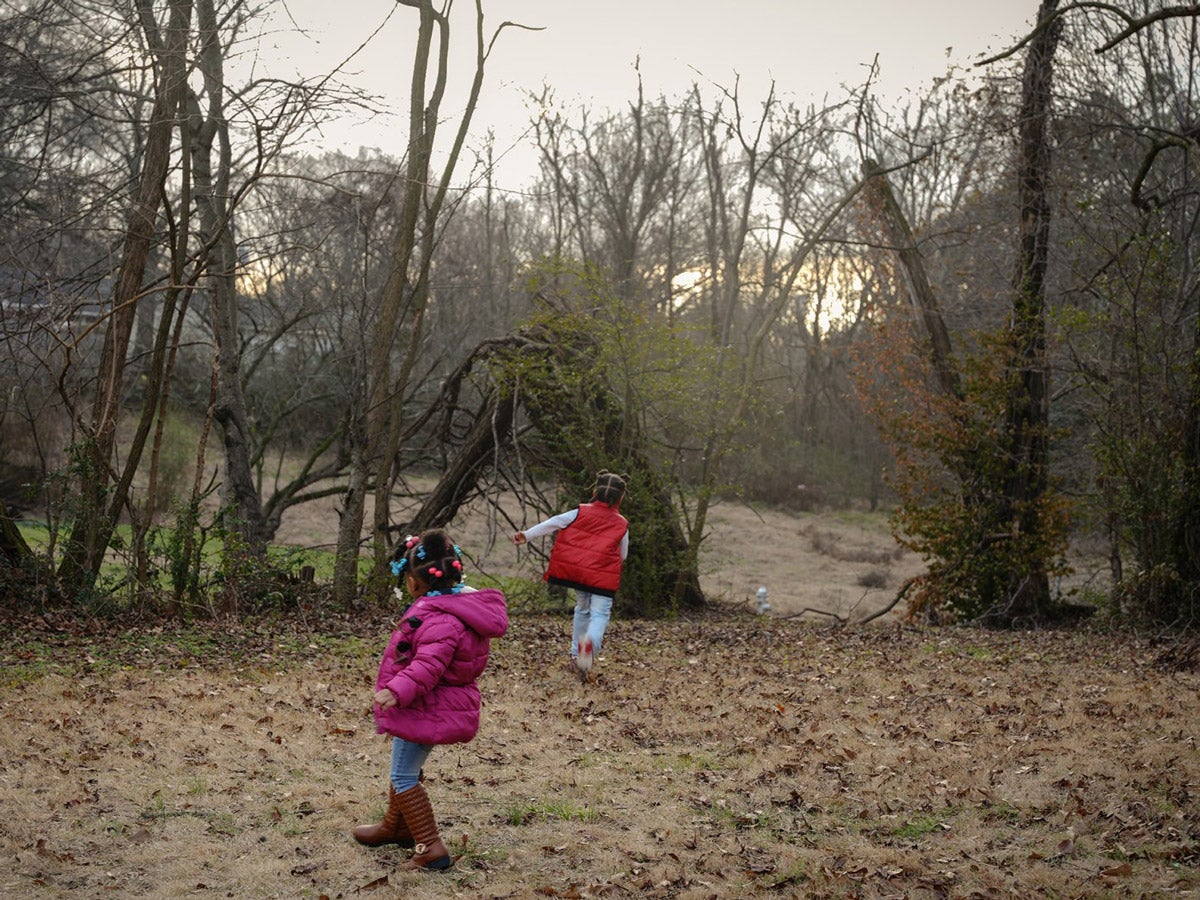 Two young black children play in their rural backyard near Memphis, Tenessee. One child wears a bright pink coat and jeans, the other a bright red vest and jeans.