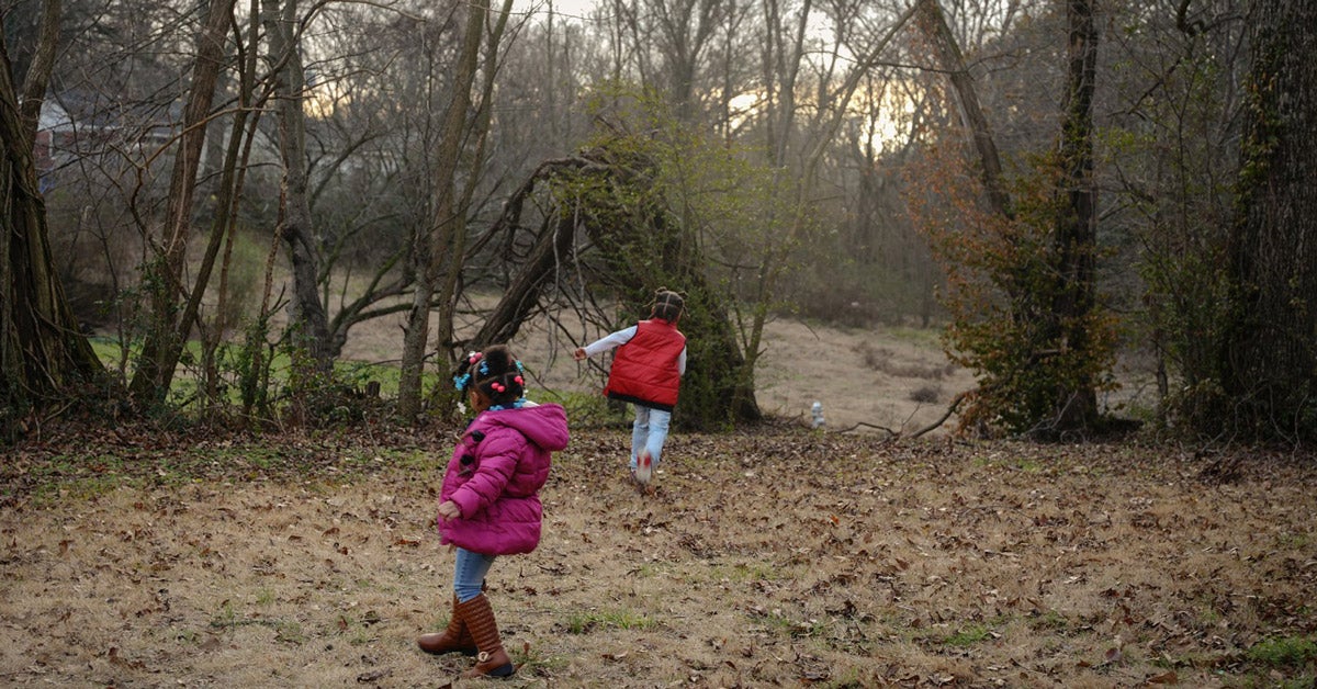 Two young black children play in their rural backyard near Memphis, Tenessee. One child wears a bright pink coat and jeans, the other a bright red vest and jeans.