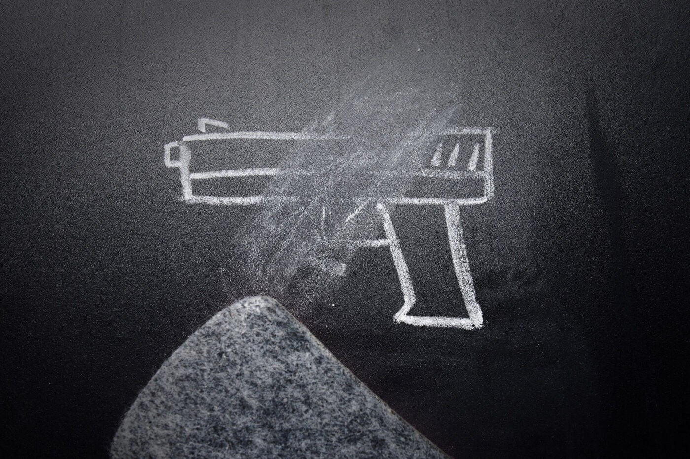 A chalk-drawn handgun being erased on a black chalkboard