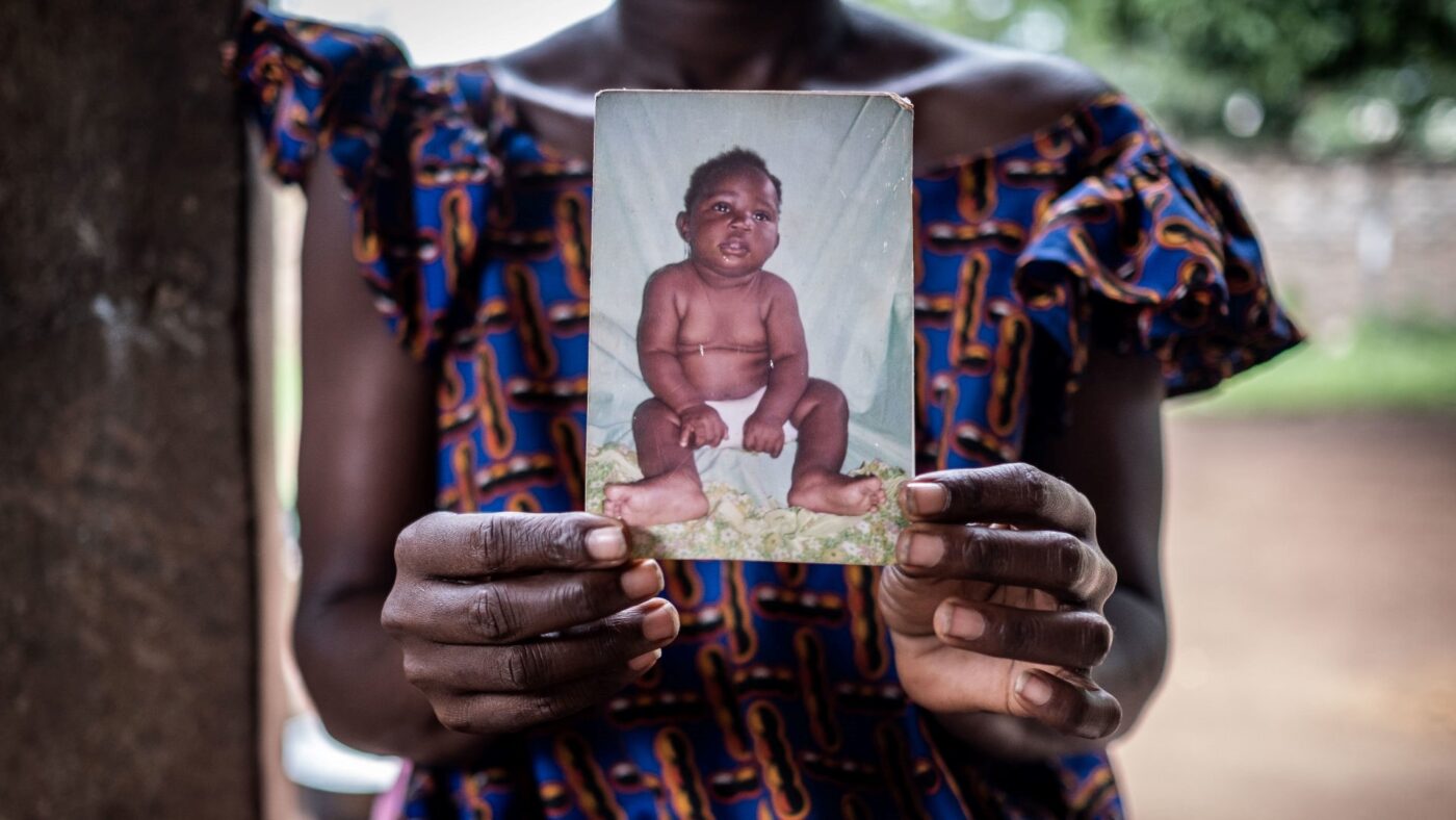 An African woman holds a worn photo of an infant in her hands.